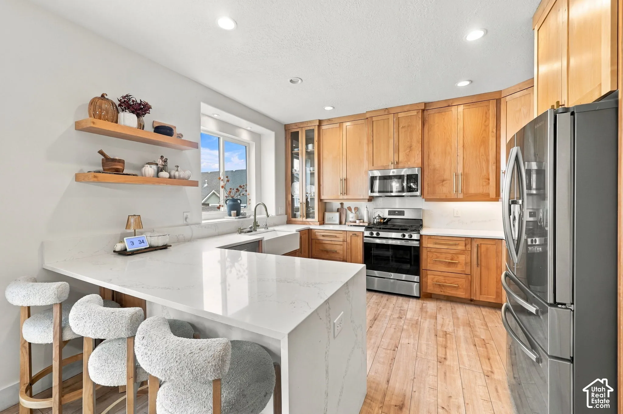 Kitchen featuring wood cabinetry, white stone-finish countertops with waterfall edge, apron-front sink, stainless steel appliances, and wood-finish flooring