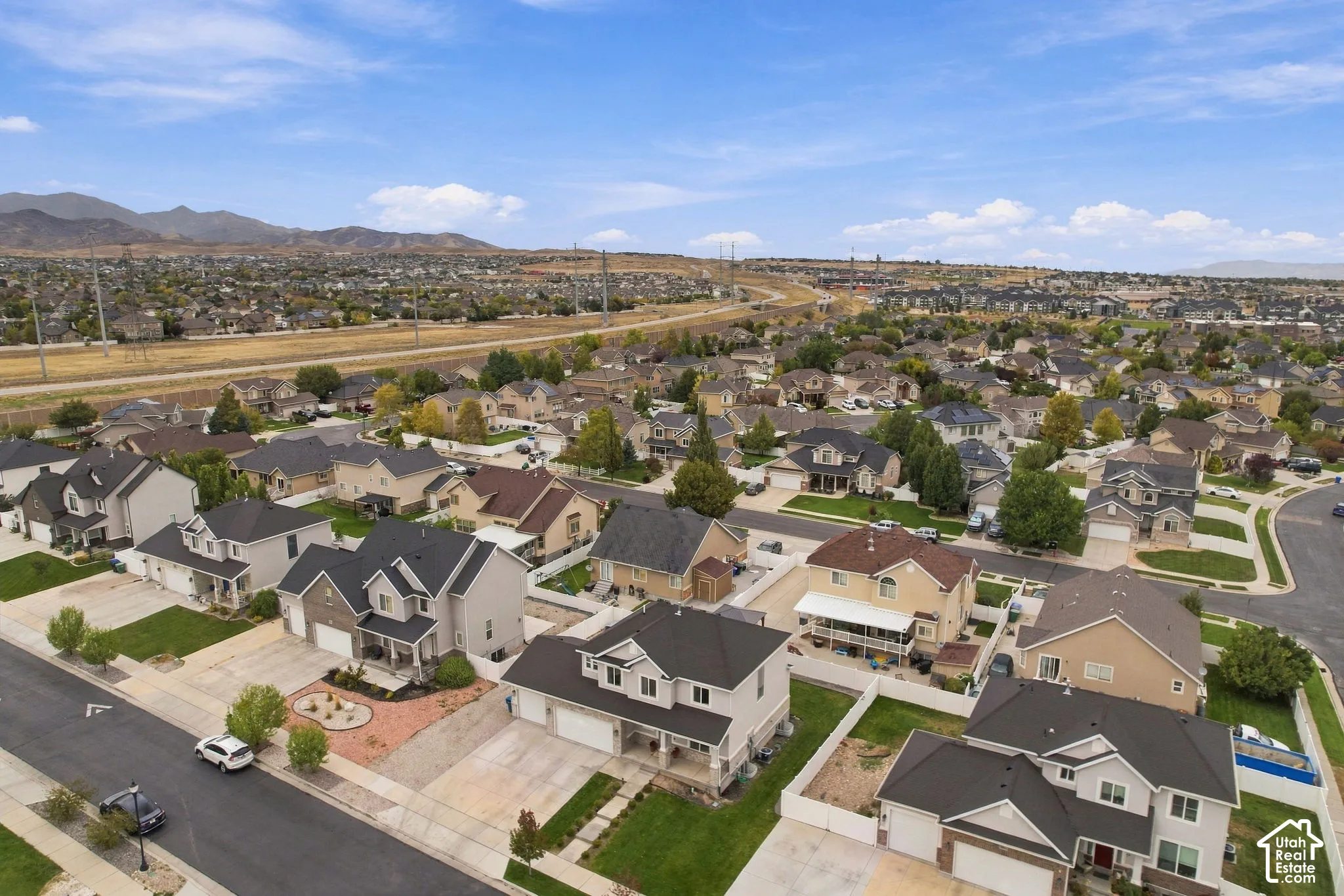 Aerial perspective featuring a multi-story residential neighborhood with paved streets, manicured lawn areas, and prominent mountain range backdrop