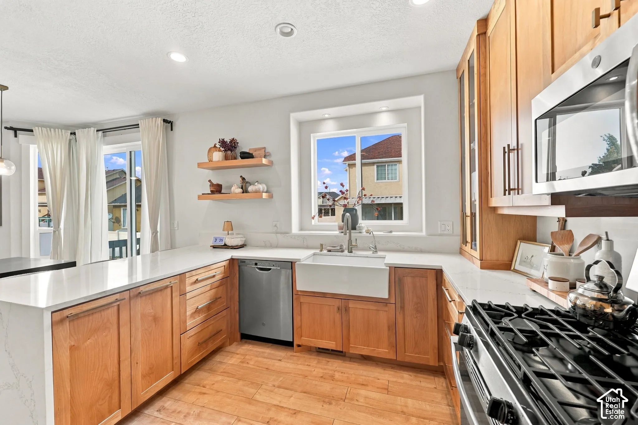 Kitchen featuring natural wood cabinetry, quartz countertops, a white farmhouse sink, stainless steel appliances, and wood-finish flooring