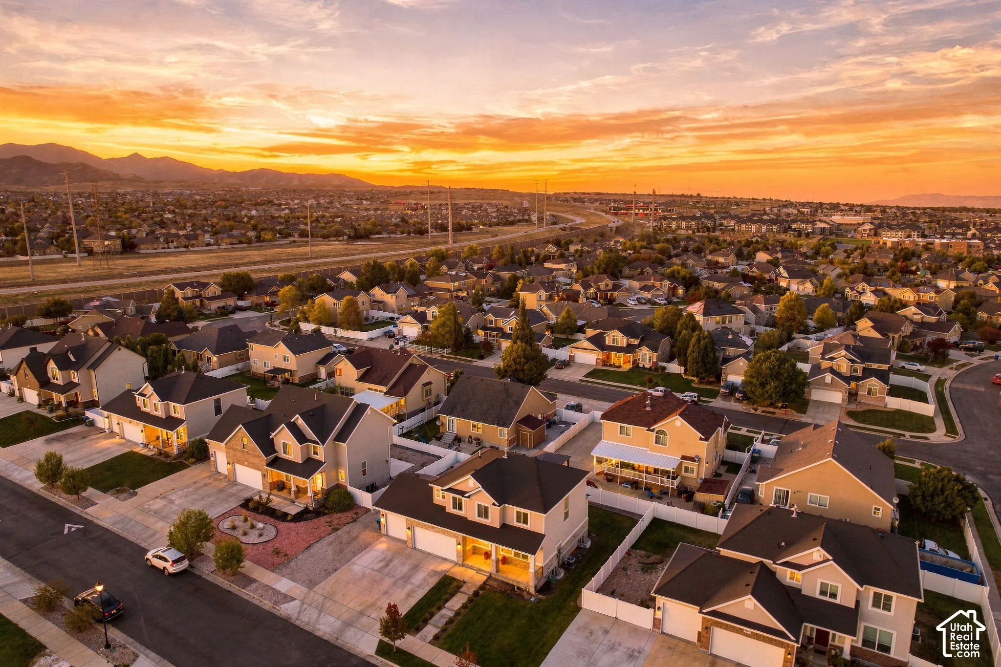 Aerial perspective featuring suburban residential development, paved streets, mountain backdrop, and golden hour sky