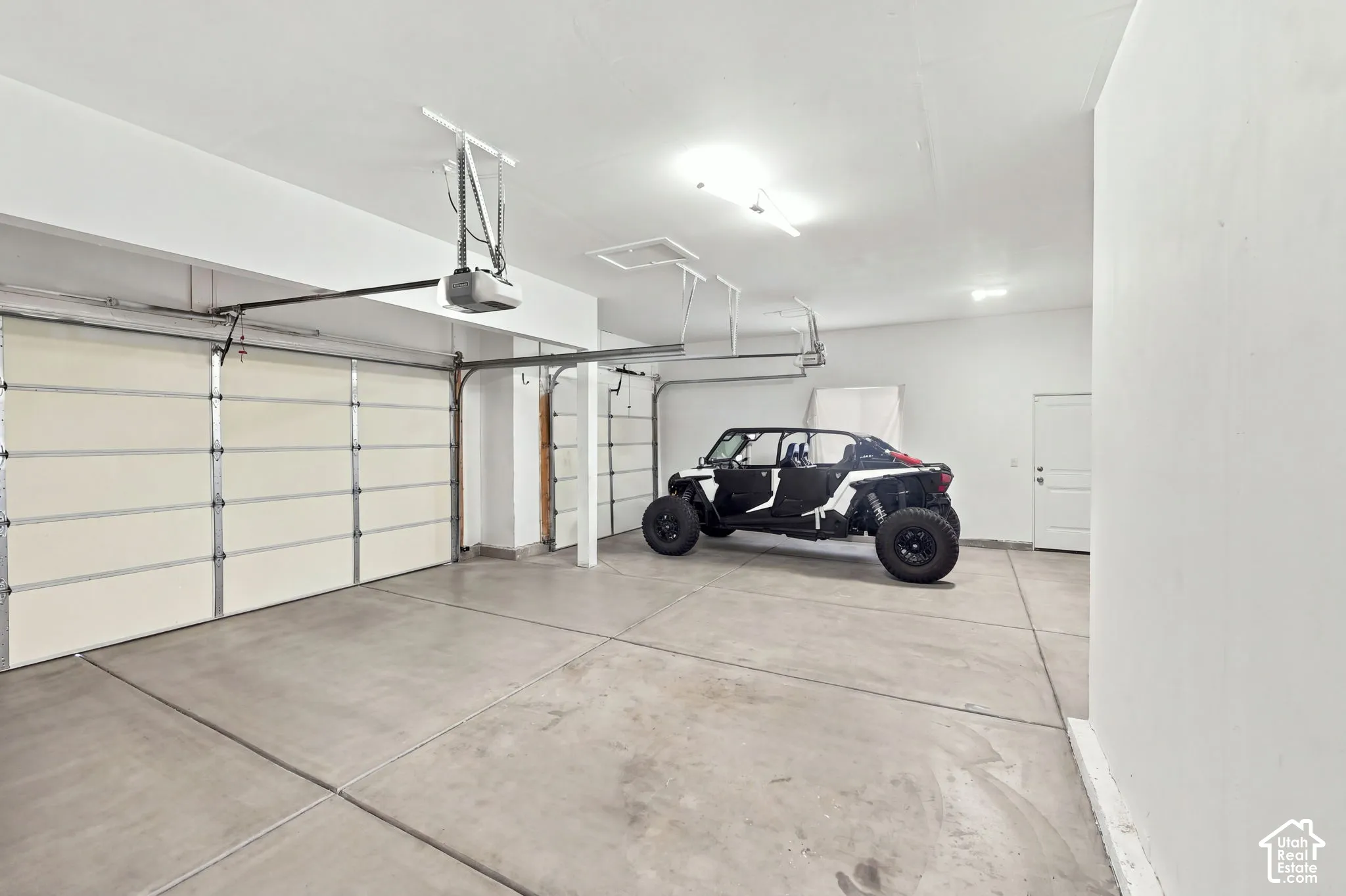 Multi-car garage featuring expansive concrete flooring, dual overhead doors, built-in automatic garage door openers, and a separate pedestrian access door