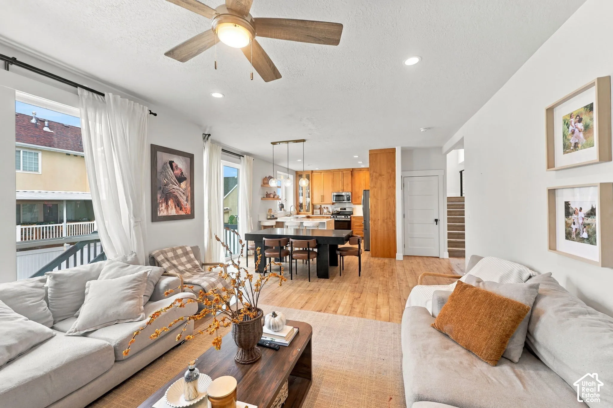 Open-concept interior featuring wood-finish flooring, a ceiling fan with integrated lighting, recessed lighting, and kitchen cabinetry with wood grain finishes