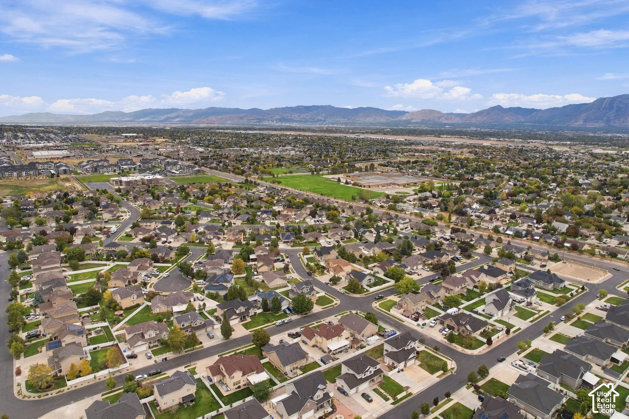 Aerial perspective of the residential area featuring paved street grids, manicured lawns, mature tree canopy, and mountainous backdrop