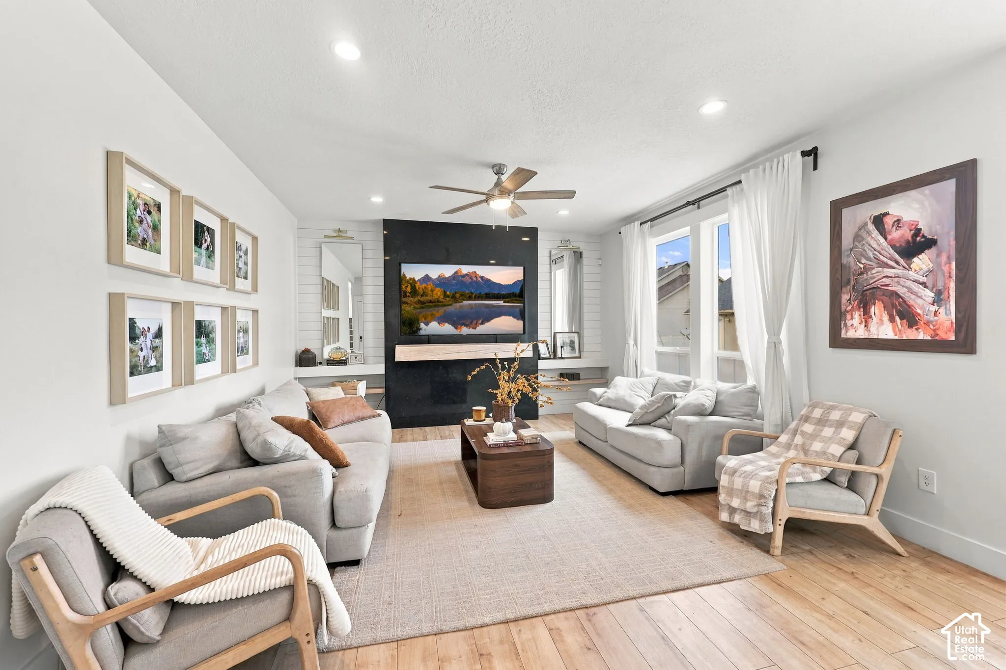 Living room featuring wood-finish flooring, a black tiled accent wall, built-in recessed shelving, a natural wood floating mantel, and recessed ceiling lighting
