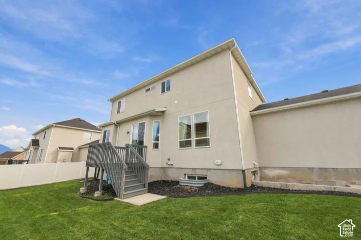 Stucco exterior with multi-level roofline, elevated wooden deck, grass lawn, and white vinyl perimeter fencing