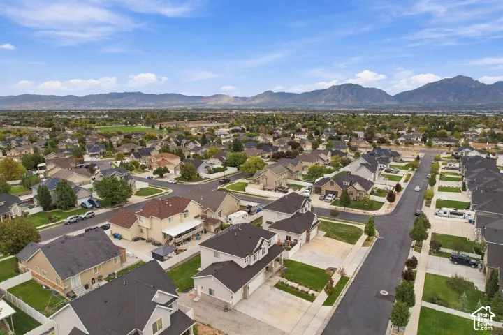 Aerial perspective of a suburban neighborhood featuring paved street grids, manicured lawns, multi-story single-family residences with pitched rooflines, and a backdrop of mountain ranges