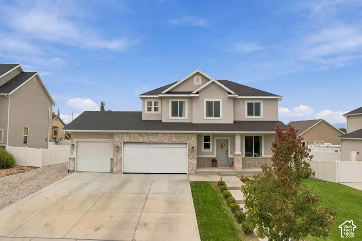 Two-story exterior featuring multi-gabled rooflines, neutral stucco siding, stone veneer accents, a three-car garage, and a concrete driveway