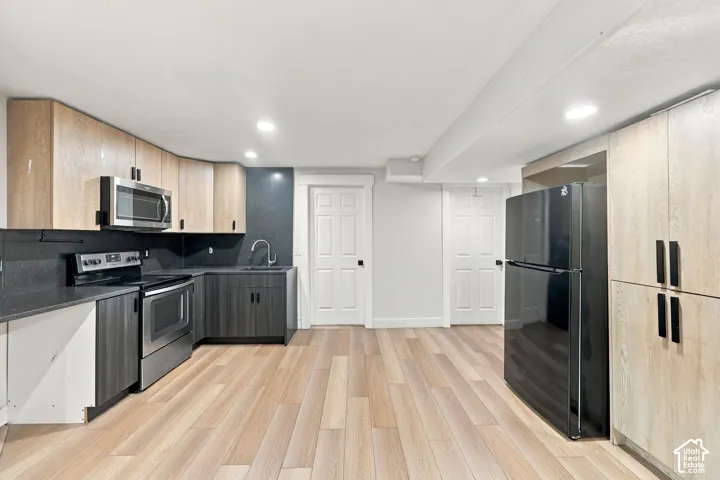 Kitchen featuring two-tone cabinetry, stainless steel appliances, dark stone-finish countertops, recessed lighting, and wood-finish flooring