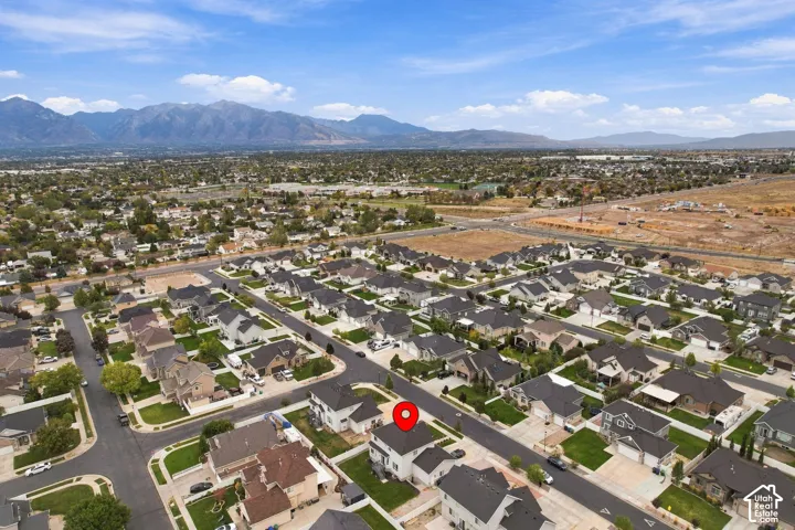 Aerial perspective featuring a two-story residence with a multi-gabled roofline and an attached garage, situated on a lot with a fenced backyard and a mountain backdrop