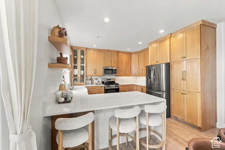 Kitchen featuring natural wood cabinetry, stone-finish countertops with a waterfall edge, stainless steel appliances, recessed ceiling lighting, and floating wood wall shelves