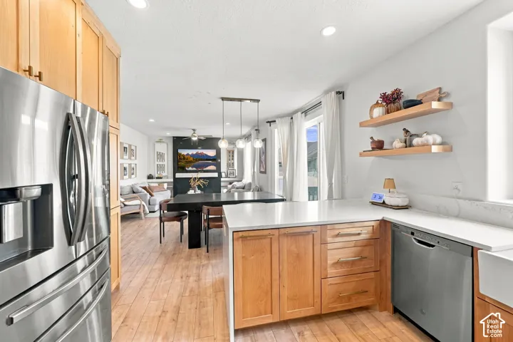 Kitchen featuring custom light wood cabinetry, stone countertops, stainless steel appliances, wood-finish flooring, and wall-mounted floating wood shelving