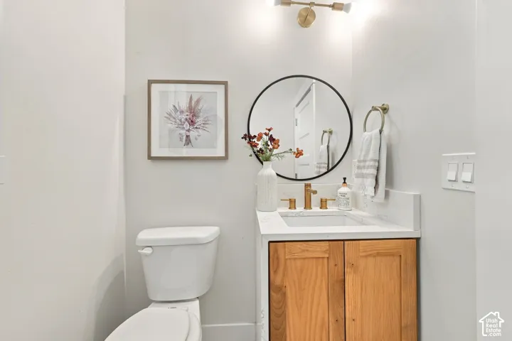 Vanity with wood-finish cabinetry, white countertop with integrated sink, brass-tone widespread faucet, round black-framed mirror, and dual-bulb wall-mounted lighting fixture
