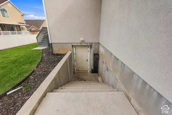 Exterior concrete staircase leading to a recessed door, stucco siding, and a landscaped yard with mulched garden beds and a white vinyl privacy fence