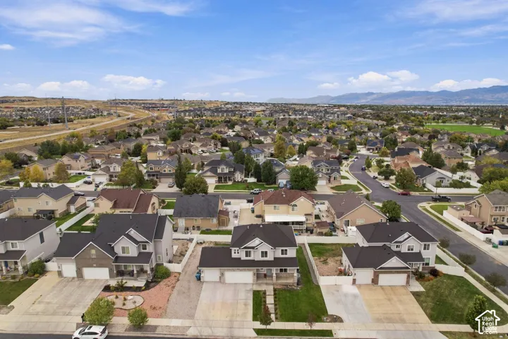 Aerial perspective of a multi-story residential property featuring a three-car garage, concrete driveway, front lawn landscaping, and white perimeter fencing