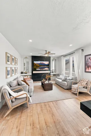 Living area featuring wood-finish flooring, a matte black tiled accent wall with integrated shelving, and recessed ceiling lighting