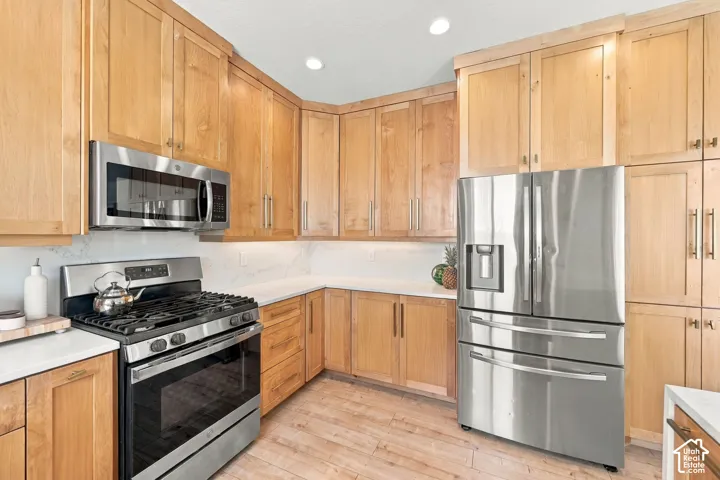 Kitchen featuring natural-finish wood cabinetry, stainless steel appliances, stone-finish countertops, recessed lighting, and wood-finish flooring