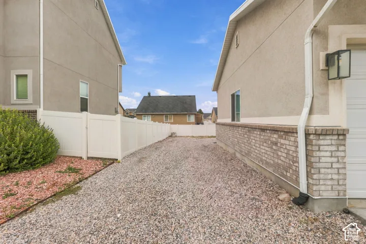 Stucco exterior with brick wainscoting, gravel side yard, and white vinyl privacy fencing