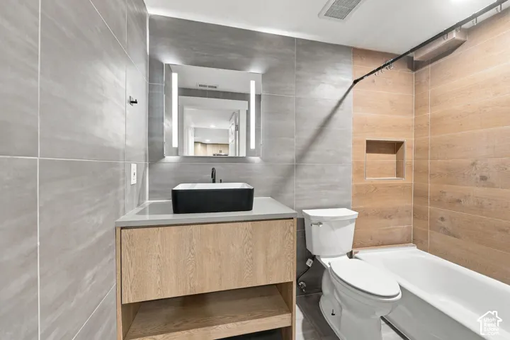 Bathroom featuring a floating wood-finish vanity, rectangular vessel sink, LED-integrated mirror, large-format grey tile walling, and wood-finish tile tub surround with a built-in recessed niche