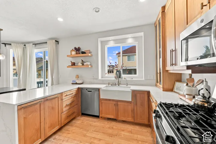 Kitchen featuring natural wood cabinetry, quartz countertops, a white farmhouse sink, stainless steel appliances, and wood-finish flooring