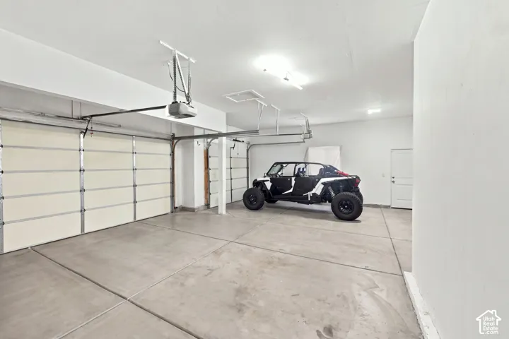 Multi-car garage featuring expansive concrete flooring, dual overhead doors, built-in automatic garage door openers, and a separate pedestrian access door