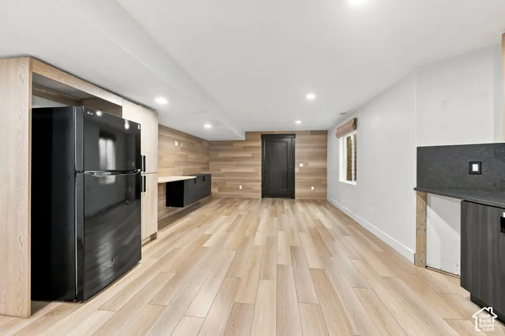 Wood-finish flooring, wood-panel accent wall, recessed lighting, matte black cabinetry, and dark stone-surface countertops