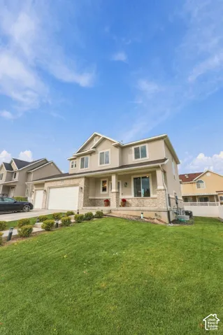 Two-story exterior featuring a stucco facade, stone veneer accents, an attached two-car garage, and a covered front porch