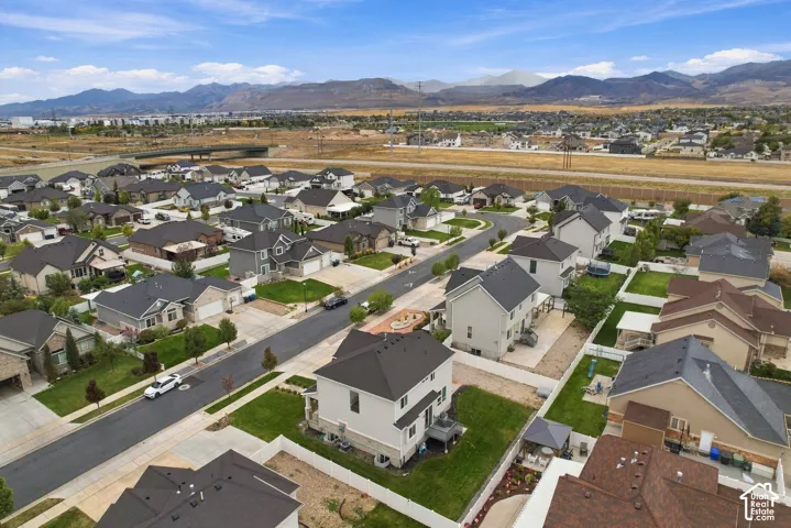 Aerial perspective of a residential community featuring multi-story dwellings, paved streets, manicured lawns, and a mountainous backdrop