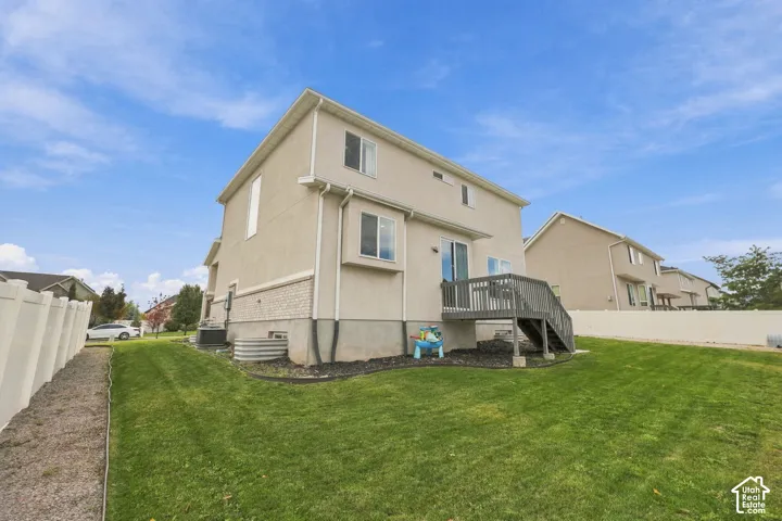 Stucco exterior featuring partial brick masonry accents, an elevated wooden deck, and a fenced backyard with lawn space