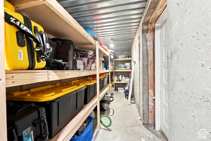 Utility room featuring concrete foundation walls, corrugated metal ceiling, concrete flooring, and built-in wooden shelving