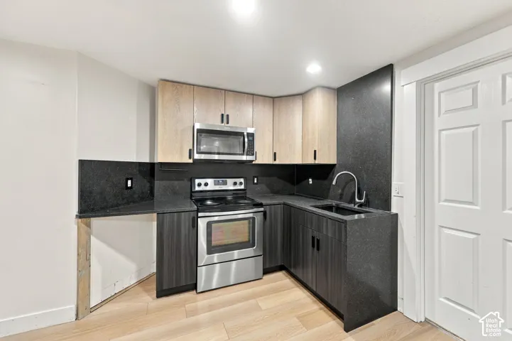 Kitchen featuring two-tone cabinetry, stainless steel oven and microwave, dark solid-surface countertops with matching full-height backsplash, undermount sink with gooseneck faucet, and wood-finish flooring