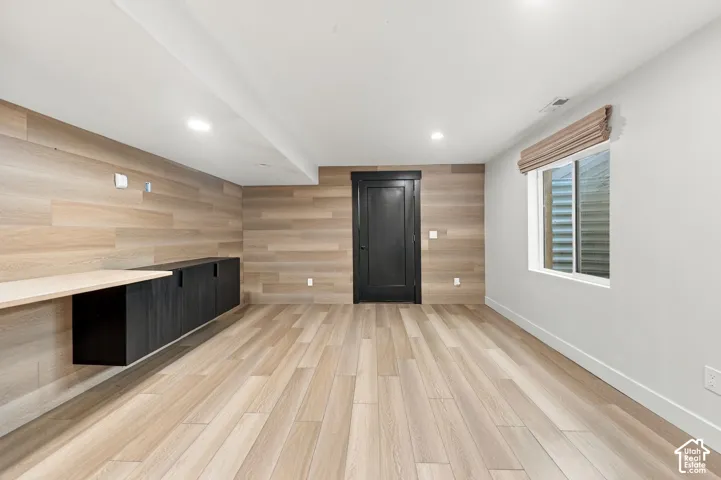 Wood-finish wall paneling, light wood-finish flooring, built-in matte black cabinetry with a light wood-finish countertop, black interior door, and recessed lighting