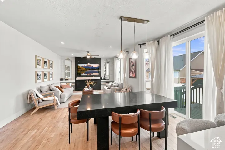 Open-concept area featuring wood-finish flooring, a contemporary three-light pendant fixture, a floor-to-ceiling fireplace surround with built-in shelving, and large sliding glass doors