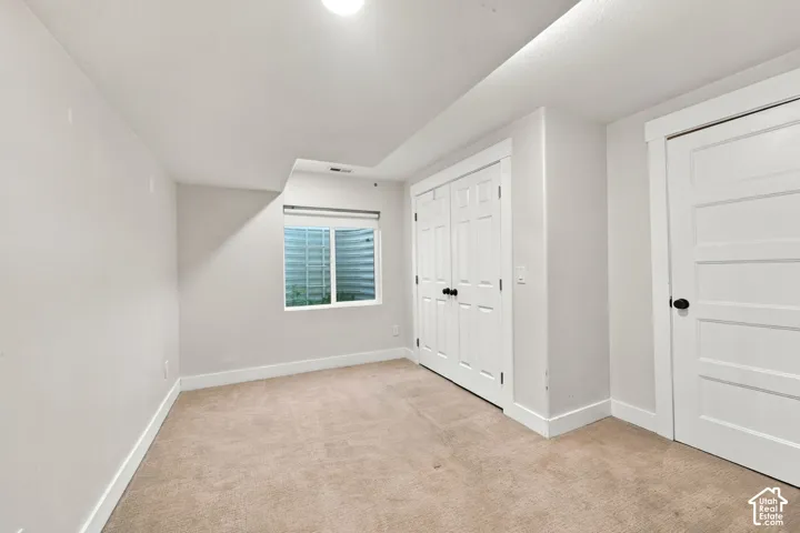 Neutral-toned interior space featuring carpeted flooring, a recessed window with a window well, double-panel closet doors, and a single-panel door with matte black hardware