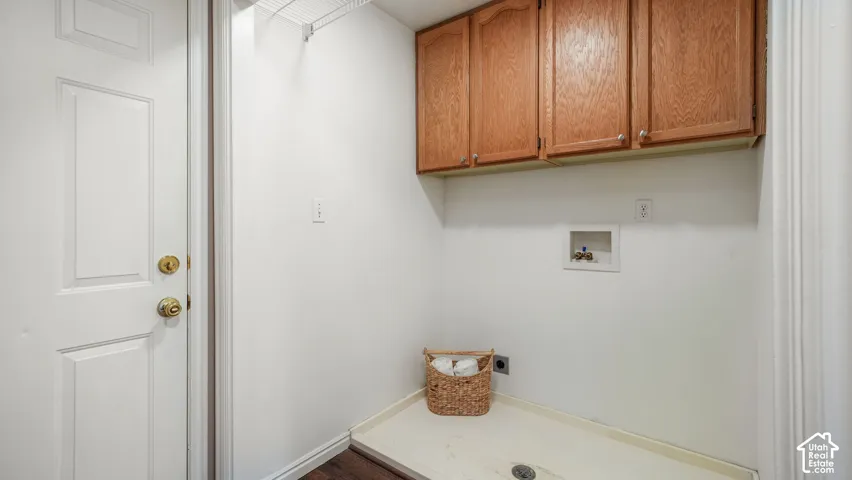 Laundry utility area featuring wood-finish upper cabinetry, a washer pan with integrated drain, and an garage access door