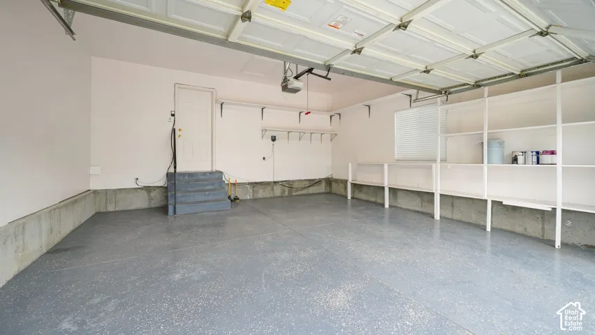 Attached garage featuring an epoxy-coated floor, integrated built-in wall shelving, an elevated pedestrian door with concrete steps, and a motorized overhead door opener