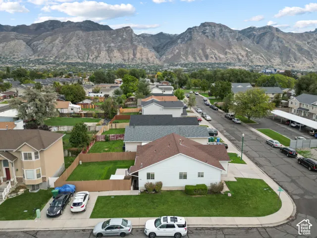 Aerial perspective featuring a corner-lot property with a fenced rear yard, asphalt driveway, extra ADU parking, and mountain backdrop
