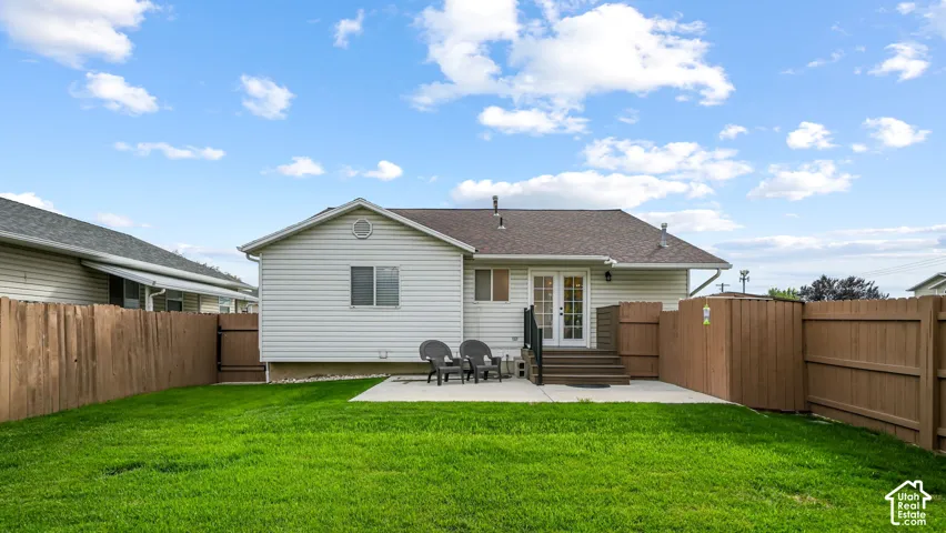 Fenced backyard featuring a manicured lawn, concrete patio, and rear entry French doors with exterior stairs