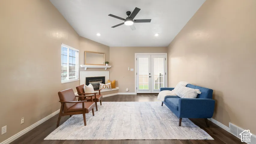 Vaulted ceilings, corner fireplace with white mantel, LVP flooring, recessed lighting, and glass-paneled double doors with in-pane blinds