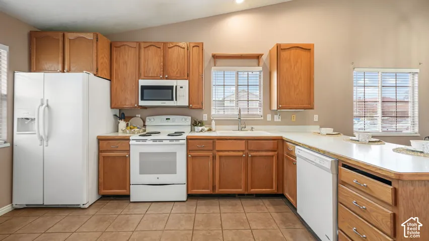 Kitchen featuring natural wood cabinetry, white appliances, a peninsula with extended counter space, vaulted ceilings, and tile flooring