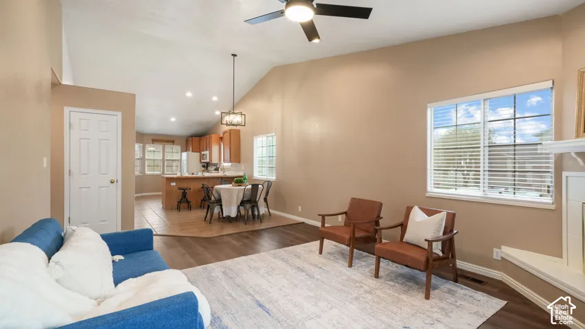 Open-concept interior featuring vaulted ceilings, LVP flooring, a kitchen peninsula, a ceiling fan, and a fireplace with a hearth