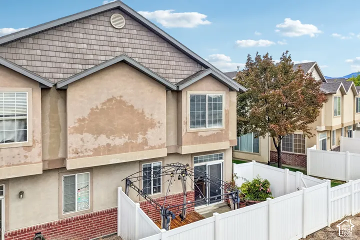 Exterior featuring stucco and shake siding, brick masonry detailing, sliding glass doors, and a private fenced outdoor area