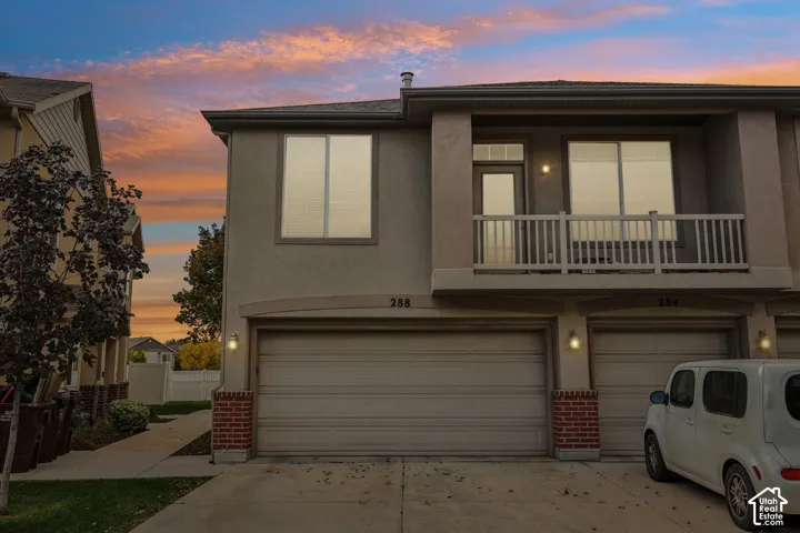 Two-story exterior featuring a stucco finish, red brick accents, an attached two-car garage, and a second-level balcony with white railings