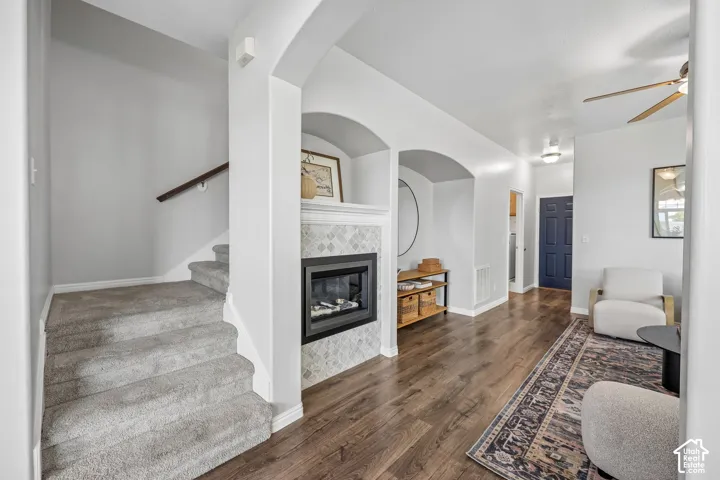 Interior featuring wood-finish flooring, a double-sided fireplace with a patterned tile surround, two built-in arched alcoves, and carpeted staircase with a wood handrail