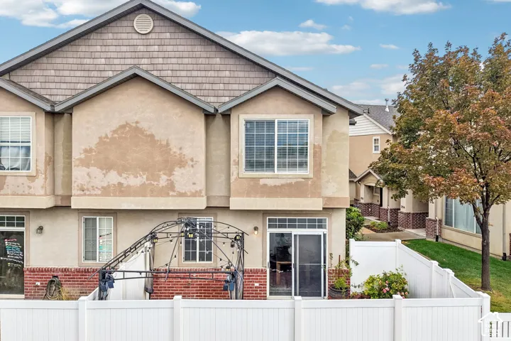Multi-level exterior featuring tan stucco siding, brown shingle gable accents, red brick masonry detailing, and a private fenced outdoor area with a sliding glass door entry