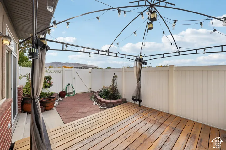 Outdoor patio featuring a wood-plank deck, red paver hardscaping, a tiered stone garden bed, and a full-height vinyl privacy fence