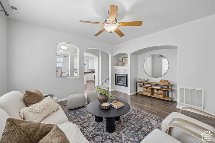 Living area featuring wood-finish flooring, a recessed fireplace with a tiled hearth, arched wall openings, and a ceiling fan with light fixture