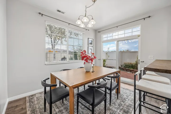 Dining area featuring wood-finish flooring, a multi-light chandelier, and large windows with horizontal blinds
