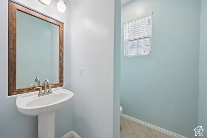 Pedestal sink with a brushed-finish faucet, framed wall-mounted mirror, multi-light vanity fixture, and tile flooring