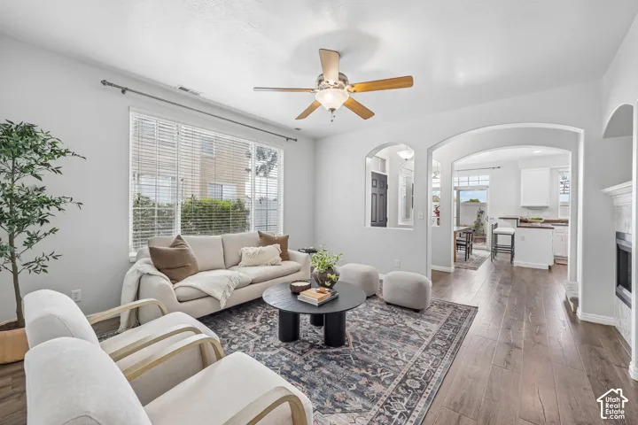 Wood-finish flooring, recessed archway openings, central ceiling fan, large picture window, and stone-surround fireplace