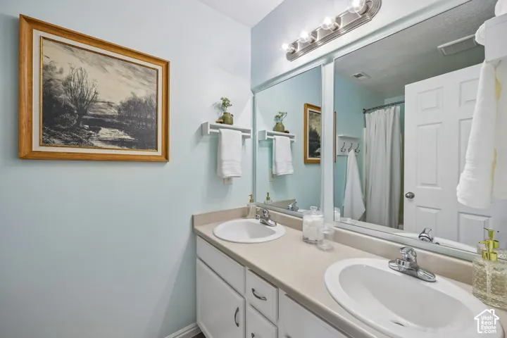 Dual-sink vanity with a solid-surface countertop, full-width wall mirror, wall-mounted light fixture, and built-in towel shelving